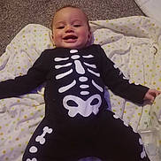 Kymarii-Axtun is registered to the contest to win money with this photo: baby, child, smiling, skeleton_outfit, black_clothing, white_bones, blanket, polka_dots, carpet, indoors, cute, happy, infant, lying_down, face, person, toddler, costume, holiday, playful