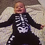 baby, child, smiling, skeleton_outfit, black_clothing, white_bones, blanket, polka_dots, carpet, indoors, cute, happy, infant, lying_down, face, person, toddler, costume, holiday, playful