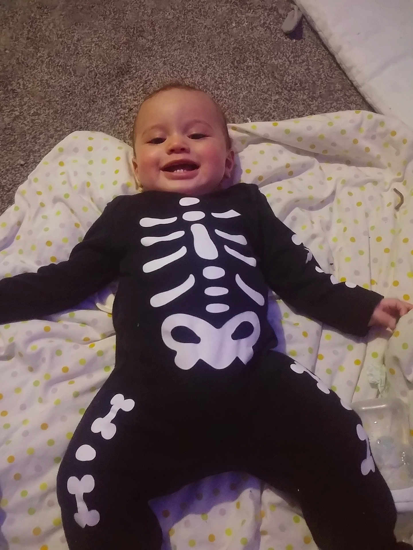 Kymarii-Axtun is registered to the contest to win money with this photo: baby, child, smiling, skeleton_outfit, black_clothing, white_bones, blanket, polka_dots, carpet, indoors, cute, happy, infant, lying_down, face, person, toddler, costume, holiday, playful