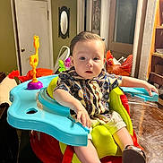 Hector is registered to the contest to win money with this photo: baby, child, indoor, seat, table, toy, colorful, shirt, curious, furniture, footwear, face, person, home, mirror, door, light, wood, patterned_clothing, expression