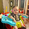 baby, child, indoor, seat, table, toy, colorful, shirt, curious, furniture, footwear, face, person, home, mirror, door, light, wood, patterned_clothing, expression