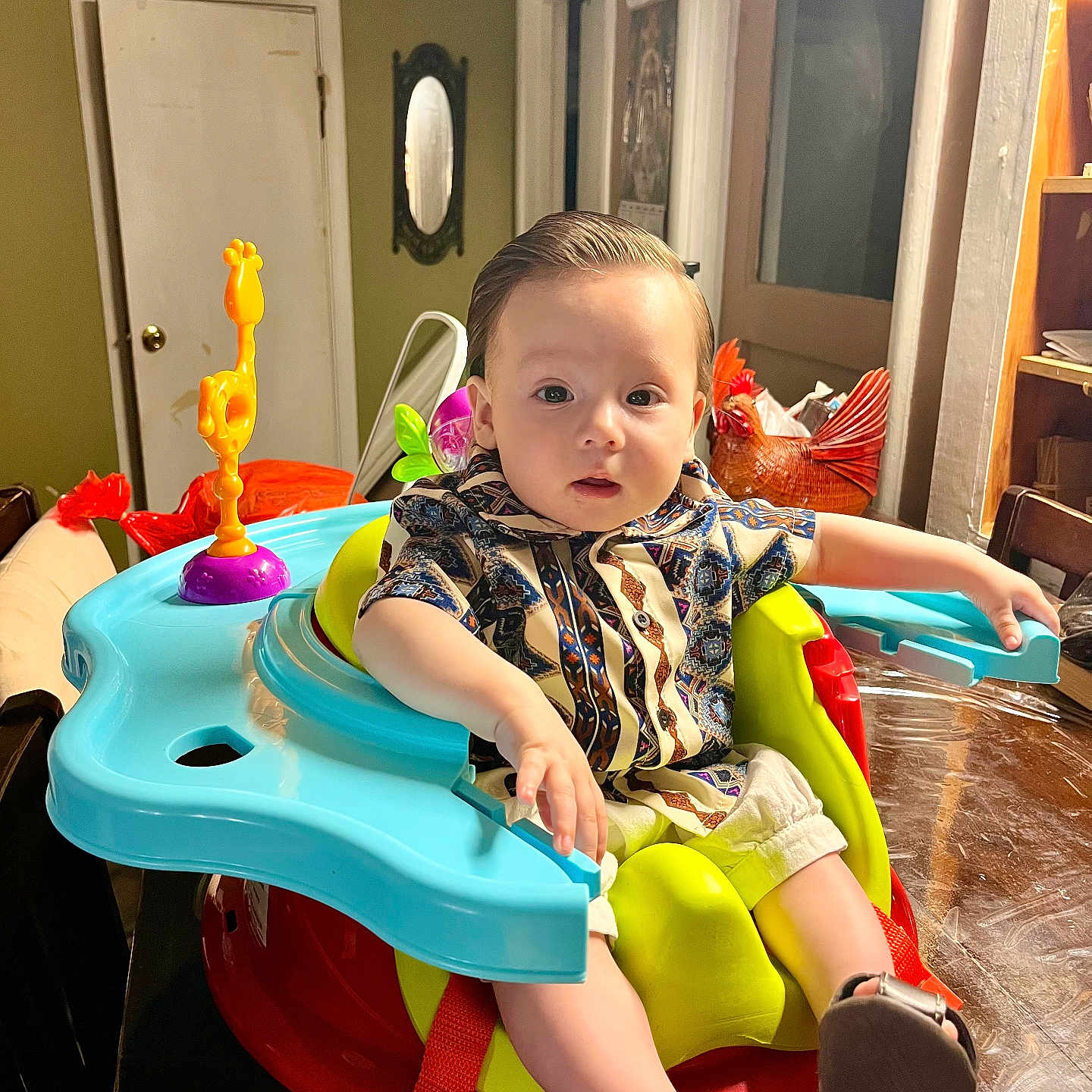 Hector is registered to the contest to win money with this photo: baby, child, indoor, seat, table, toy, colorful, shirt, curious, furniture, footwear, face, person, home, mirror, door, light, wood, patterned_clothing, expression