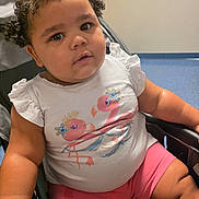 Alisha joined the competition — help win amazing prizes! toddler, child, curly_hair, stroller, pink_shorts, white_shirt, flamingo_print, indoors, cute, chubby_cheeks, seated, person, baby, casual_clothing, curious_expression, furniture, soft_lighting, portrait, young_child, comfortable