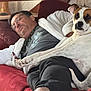 man, dog, couch, sleeping, relaxed, indoor, robe, glasses, barefoot, white_dog, brown_spot, paw, home, casual, comfort, resting, furniture, human, pet, lifestyle