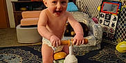 Garreth is registered to the contest to win money with this photo: activity, baby_gate, barefoot, blur, carpet, child, diaper, floor, furniture, home, indoor, living_room, person, playful, smiling, television, toddler, toy, tricycle, video_game
