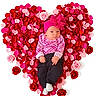 baby, infant, pink_hat, plaid_shirt, black_pants, white_socks, rose_petals, heart_shape, red_roses, pink_roses, flower_arrangement, valentine_theme, cute, portrait, laying_down, studio_photo, white_background, adorable, child, newborn