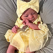 Aurora joined the competition — help win amazing prizes! baby, infant, yellow_dress, headband, bow, polka_dot, cushion, sleepy, cute, small_feet, newborn, soft, indoors, child, person, apparel, fabric, relaxing, resting, cozy