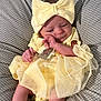 baby, infant, yellow_dress, headband, bow, polka_dot, cushion, sleepy, cute, small_feet, newborn, soft, indoors, child, person, apparel, fabric, relaxing, resting, cozy