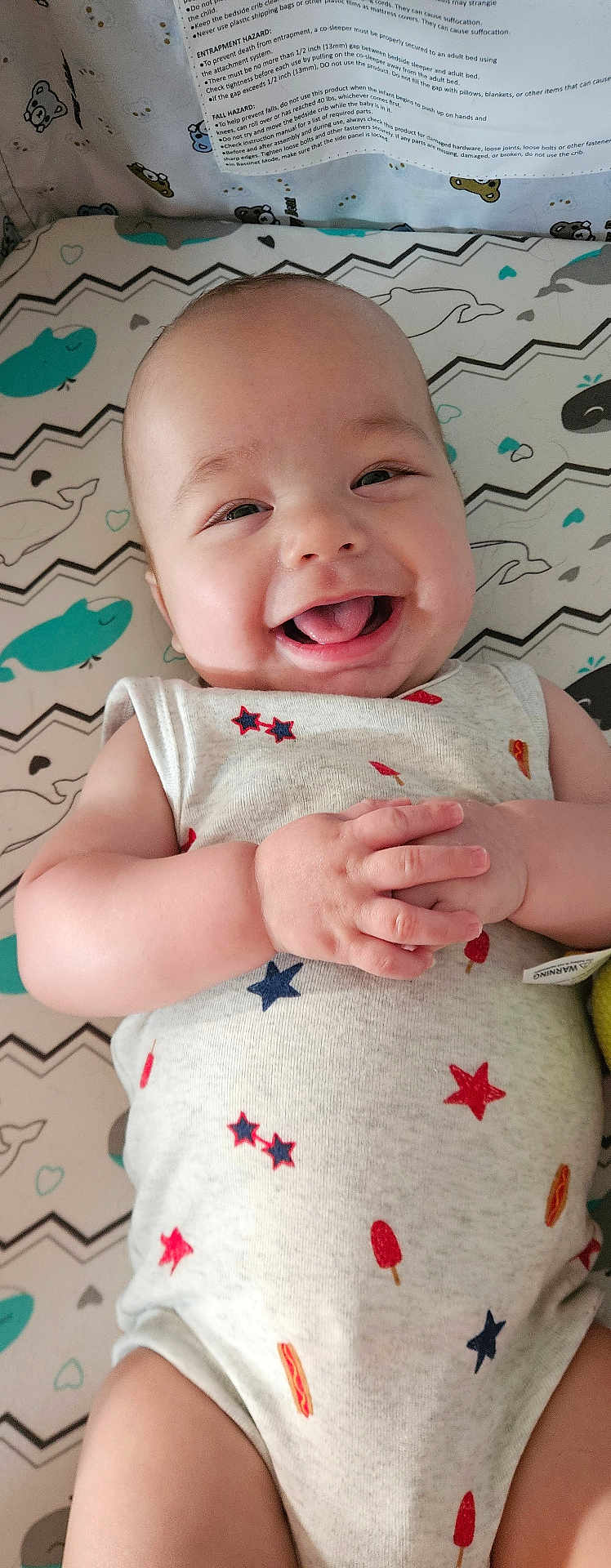 Jason joined the competition — help win amazing prizes! baby, smiling, infant, onesie, patterned_clothing, hands, tongue_out, lying_down, mattress, whale_pattern, zigzag_pattern, cute, happy, child, indoor, closeup, skin, head, face, playful