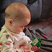 Callan is registered to the contest to win money with this photo: baby, blanket, child, christmas, couch, cozy, curious, cute, exploring, face, gift_bow, hands, holiday, holiday_theme, indoor, infant, pajamas, sitting, soft_lighting, young_child