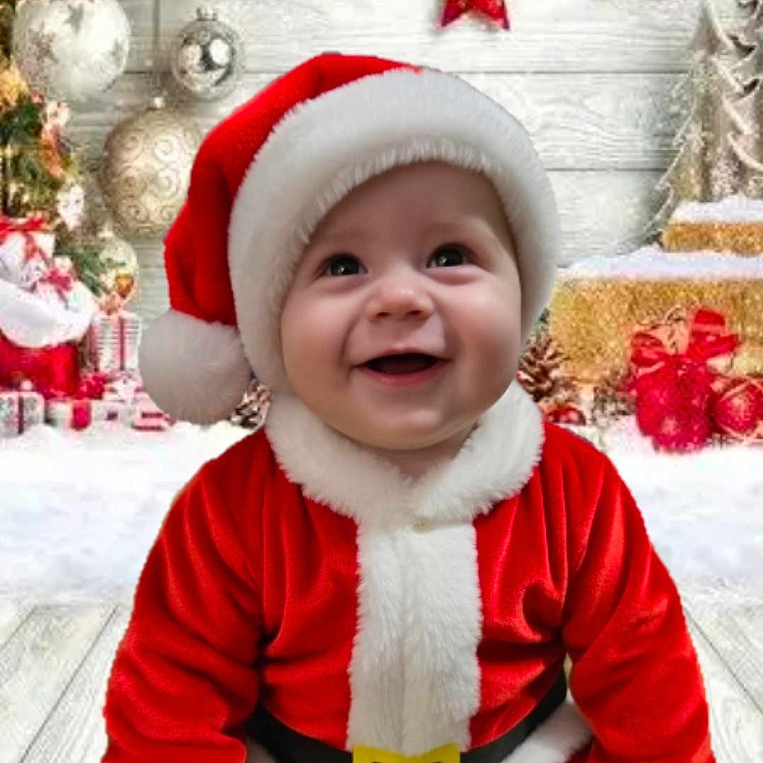 Callan is registered to the contest to win money with this photo: baby, background, belt, celebration, child, christmas, cute, decorations, festive, floor, holiday, indoor, ornaments, presents, red, red_hat, santa_claus_costume, smiling, white_fur, wooden_floor