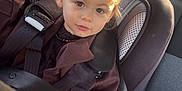 Swann a rejoint le concours — aidez-le/la à gagner de superbes lots ! airbag_label, brown_coat, buckled_up, car_interior, car_seat, child, cozy, expression_neutral, eyes, face, hair_bun, headrest, necklace, portrait, rear_seat, safety, seatbelt, sunlight, toddler, window_light