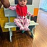 baby, child, infant, sitting, bench, bib, pacifier, pajamas, hello_kitty, pink_clothing, red_bib, portrait, indoor, colorful_background, wooden_floor, adult_hand, support, cute, face, furniture