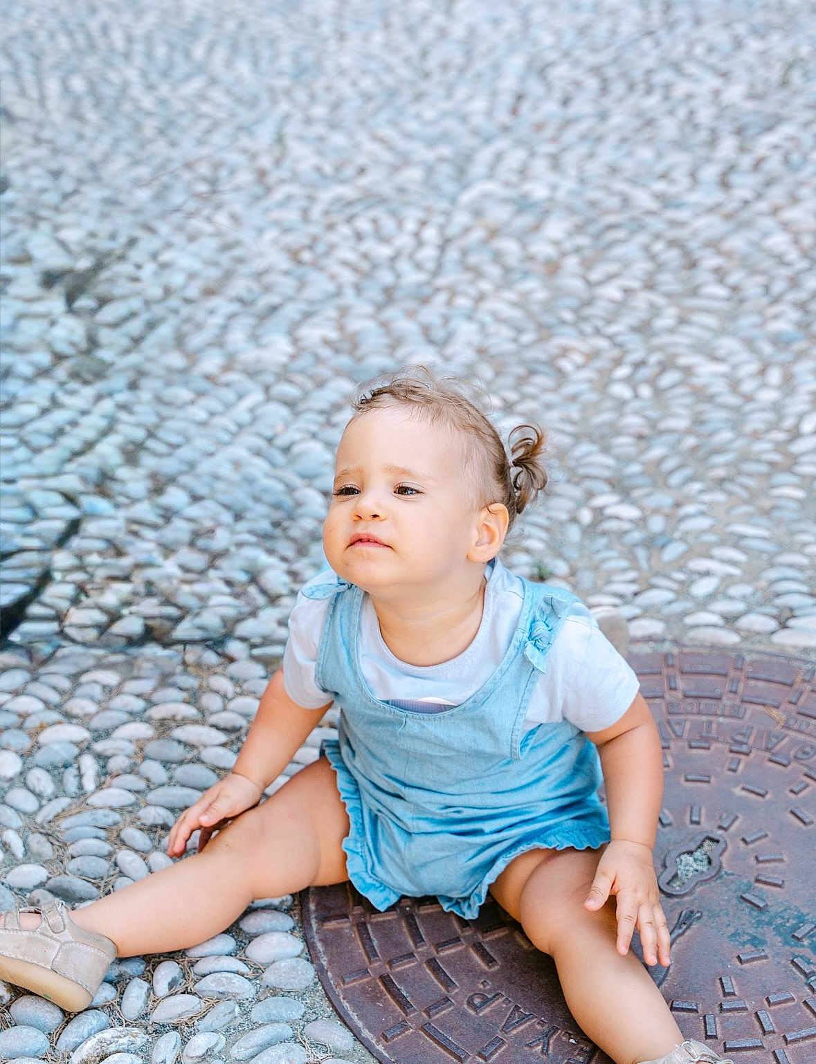 Victoire participe au concours pour gagner de l'argent avec cette photo : toddler, child, sitting, cobblestone, manhole_cover, blue_dress, white_shirt, shoes, outdoor, curly_hair, pony_tail, legs_spread, street, casual, daylight, young_child, person, cute, expression, side_view