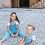 child, children, toddler, sitting, outdoor, cobblestone, stone_wall, archway, gate, blue_outfit, shorts, overalls, white_shirt, footwear, smile, hair, person, daylight, urban, casual