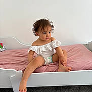Skylar joined the competition — help win amazing prizes! toddler, child, bed, white_bed, pink_sheet, curly_hair, diaper, off_shoulder_top, indoor, carpet, purple_ball, furniture, young_child, sitting, portrait, cute, skin, floor, looking_away, baby