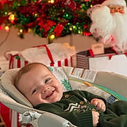 Rowan is registered to the contest to win money with this photo: baby, smiling, infant, baby_seat, christmas_tree, christmas_lights, ornaments, santa_decoration, holiday, festive, gift_boxes, red, green, indoors, happy, child, cute, seasonal, cozy, celebration