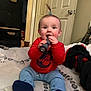 baby, child, infant, sitting, red_sweater, blue_pants, flashlight, bed, indoors, door, clothing, footwear, smiling, happy, person, room, furniture, pony_tail, toy, casual