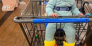 Ava joined the competition — help win amazing prizes! baby, shopping_cart, store, floor, yellow_slippers, duck_feet, onesie, child, happy, smiling, indoor, retail, clothing, person, seatbelt, toy, flooring, aisle, shopping, cute