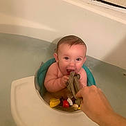 Ava joined the competition — help win amazing prizes! baby, bathtub, water, bath_seat, toy, hand, cloth, smiling, child, indoor, bath_time, playful, happy, person, skin, head, face, arm, tile, bathroom