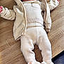 baby, child, infant, knitwear, beanie, slippers, bunny_slippers, table, wooden_table, floor, tile_floor, clothing, warm_clothing, cute, lying_down, indoors, soft_texture, cozy, face, expression