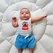 Arthur participe au concours pour gagner de l'argent avec cette photo : baby, infant, cute, smiling, blue_shorts, striped_tank_top, red_crab, cushion, white_fluffy, lying_down, indoors, child, portrait, happy, skin, face, arm, legs, footwear_free, soft