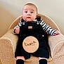baby, child, infant, overalls, striped_shirt, armchair, plaque, wooden, socks, floor, cute, portrait, indoor, furniture, sitting, person, young, expression, cozy, clothing