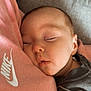 baby, sleeping, face, pink_sweatshirt, nike_logo, gray_clothing, cushion, cozy, peaceful, infant, closeup, resting, soft_lighting, portrait, child, cute, warm, indoors, comfort, tender