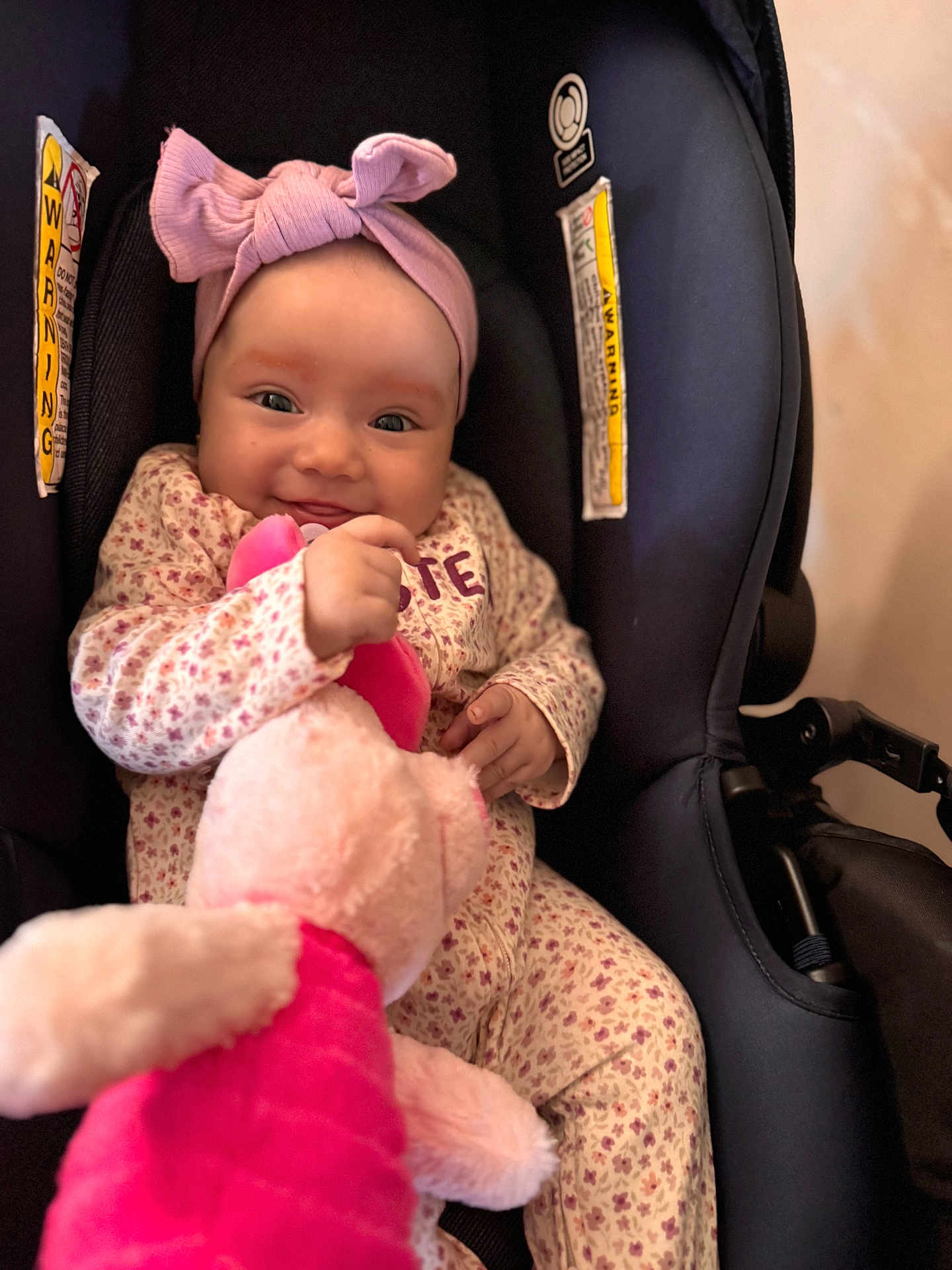 Chloe joined the competition — help win amazing prizes! baby, infant, child, car_seat, pink_headband, bow, floral_pajamas, stuffed_animal, toy, smiling, happy, cute, indoors, seatbelt, child_safety, portrait, closeup, person, young, comfort