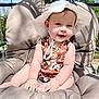 baby, child, smiling, hat, sun_hat, floral_dress, outdoor, swing, cushion, seat, sunlight, happy, cute, infant, summer, nature, greenery, portrait, baby_hands, baby_feet