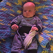 James joined the competition — help win amazing prizes! baby, infant, onesie, blanket, knit_blanket, soft_toy, clothing, person, indoor, cute, child, newborn, hand, face, head, sitting, comfort, pattern, colorful, cozy