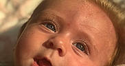 Everly is registered to the contest to win money with this photo: baby, blanket, blue_eyes, child, close_up, clothing, cute, expression, eyelashes, face, golden_hair, indoors, infant, mouth_open, newborn, portrait, skin, sleepwear, soft_light, warm_light