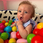 Everly is registered to the contest to win money with this photo: baby, ball_pit, blue, blue_eyes, child, clothing, colorful_balls, cute, green, indoor, person, pink, play, playpen, portrait, purple, red, surprised_expression, toddler, yellow