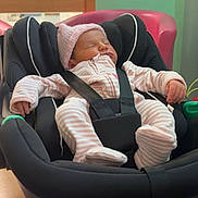 Elsi-Mae is registered to the contest to win money with this photo: baby, newborn, car_seat, sleeping, infant, pink_clothing, knitted_hat, straps, indoor, wooden_table, soft_lighting, peaceful, child, person, seat, baby_clothes, cute, resting, young_child, cozy