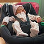 baby, newborn, car_seat, sleeping, infant, pink_clothing, knitted_hat, straps, indoor, wooden_table, soft_lighting, peaceful, child, person, seat, baby_clothes, cute, resting, young_child, cozy