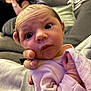 Elsi-Mae joined the competition — help win amazing prizes! baby, infant, person, hand, face, pink_clothing, blanket, couch, blurred_background, adult, indoor, close_up, wide_eyes, curious, soft_light, skin, head_support, cozy, seated, family