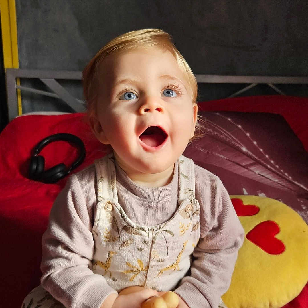 Pablo participe au concours pour gagner de l'argent avec cette photo : baby, bodypart, clothing, couch, cutlery, face, finger, furniture, hand, happy, head, indoors, laughing, pants, person, photography, portrait, quilt, sitting, spoon