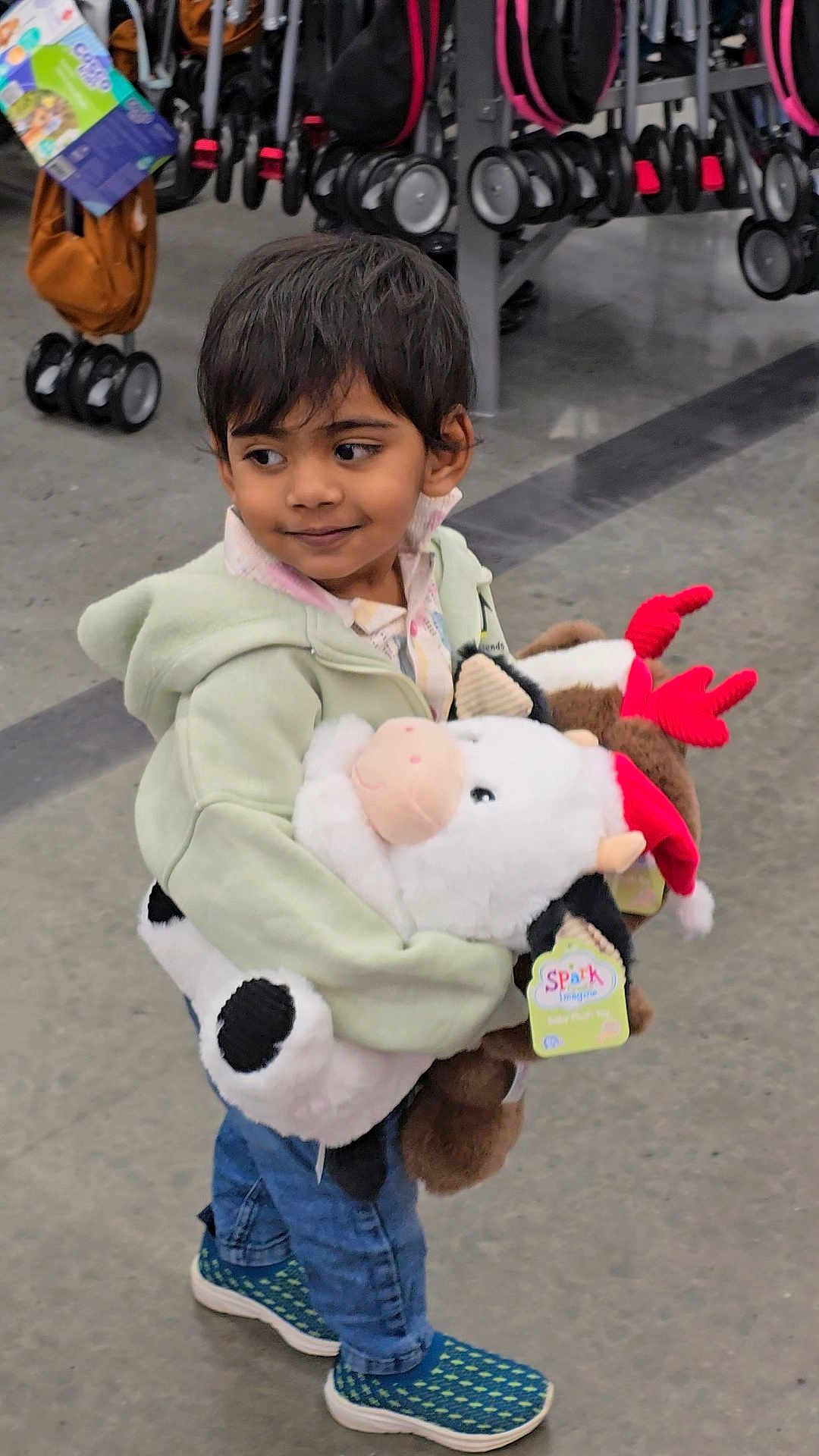 Harshiv is registered to the contest to win money with this photo: child, kid, plush_toy, cow, reindeer, red_antlers, green_hoodie, jeans, sneakers, store, shopping, strollers, aisle, floor, smile, cute, toy, holding, indoor, person