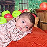 Heaven is registered to the contest to win money with this photo: baby, child, infant, portrait, lying_down, wide_eyes, floral_outfit, pink_clothing, red_blanket, apples, green_apples, red_apples, fruit, lantern, wooden_crate, indoor, colorful, close_up, face, photography