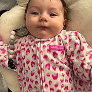 Ryleigh is registered to the contest to win money with this photo: baby, infant, face, onesie, pink, leopard_print, pacifier, pillow, soft_texture, clothing, cute, child, portrait, lying_down, indoor, young_child, calm, beads, closeup, person