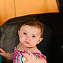 baby, child, infant, person, face, hand, striped_clothing, colorful, sitting, indoor, portrait, blue_eyes, curly_hair, young_child, table, blurry_background, string_lights, soft_lighting, expression, closeup