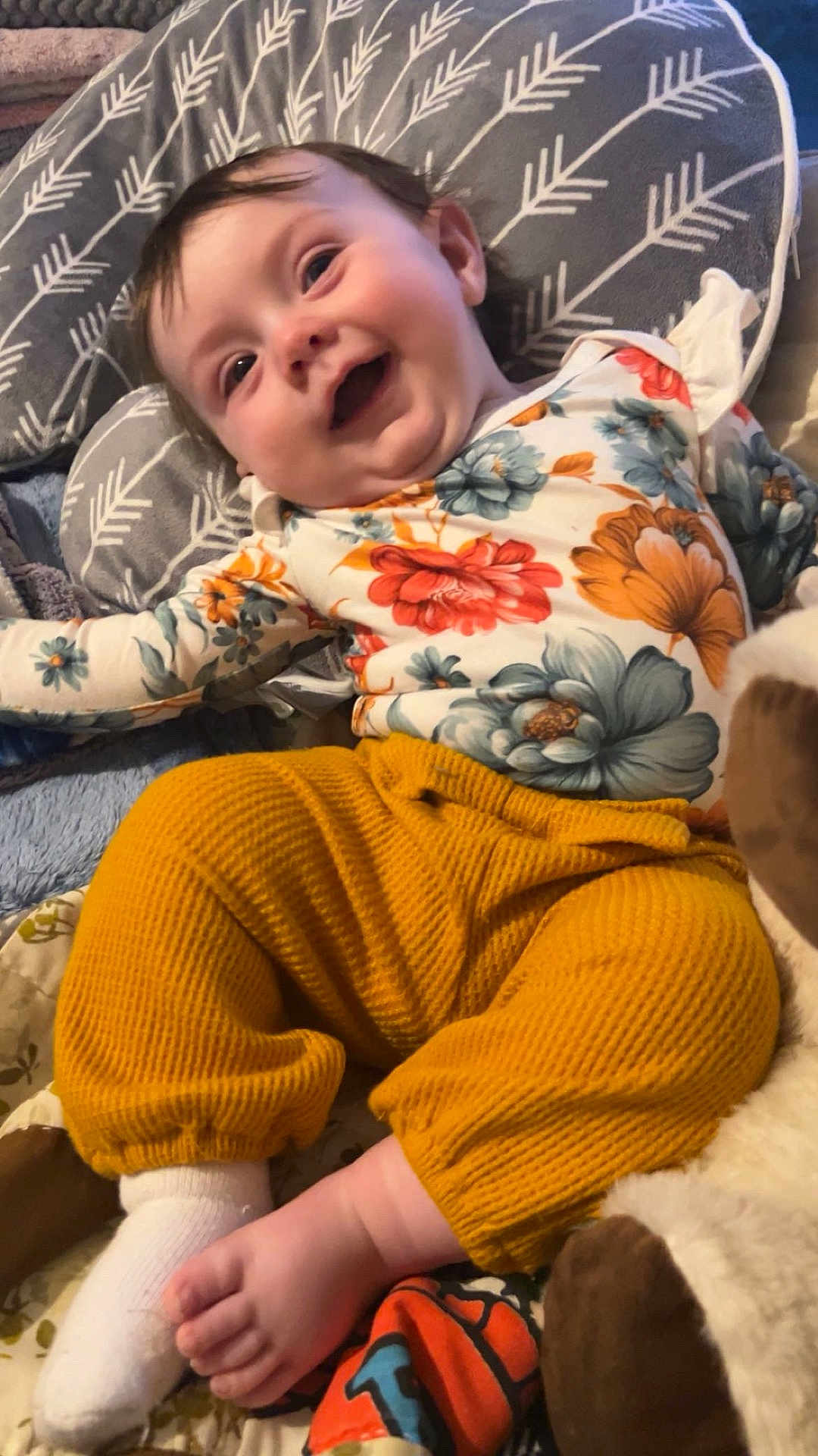 Ryleigh is registered to the contest to win money with this photo: baby, infant, smiling, happy, child, floral_shirt, yellow_pants, sock, foot, cushion, pattern, indoor, soft_toy, plush, cute, portrait, clothing, comfort, relaxed, playful