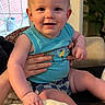 baby, child, infant, smiling, blue_shirt, checkered_shorts, blanket, hand, indoor, door, glass_door, plant, couch, person, face, happy, blonde_hair, seated, home_interior, toddler