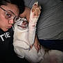 Wynter is registered to the contest to win money with this photo: person, dog, glasses, bed, cuddling, paw, smile, white_dog, nose_ring, casual_clothing, indoors, face, lying_down, human_hand, pet, canine, closeup, affection, resting, dark_background