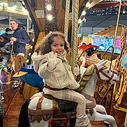 Laora participe au concours pour gagner de l'argent avec cette photo : child, carousel, merry_go_round, carousel_horse, smiling, wave, curly_hair, winter_coat, gloves, festive_lights, wooden_floor, amusement_ride, pole, crowd, man, child_face, holiday_market, seat, playful, family_outing