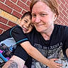child, woman, smile, hug, selfie, brick_wall, tattoo, short_hair, casual_clothing, outdoor, closeup, portrait, happy, affection, family, arm, graphic_tshirt, redhead, candid, friendship