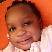 Iris a rejoint le concours — aidez-le/la à gagner de superbes lots ! baby, smile, face, child, infant, portrait, closeup, braids, cushion, orange, pink_clothing, necklace, earring, happy, indoors, person, cute, young_child, soft_lighting, resting