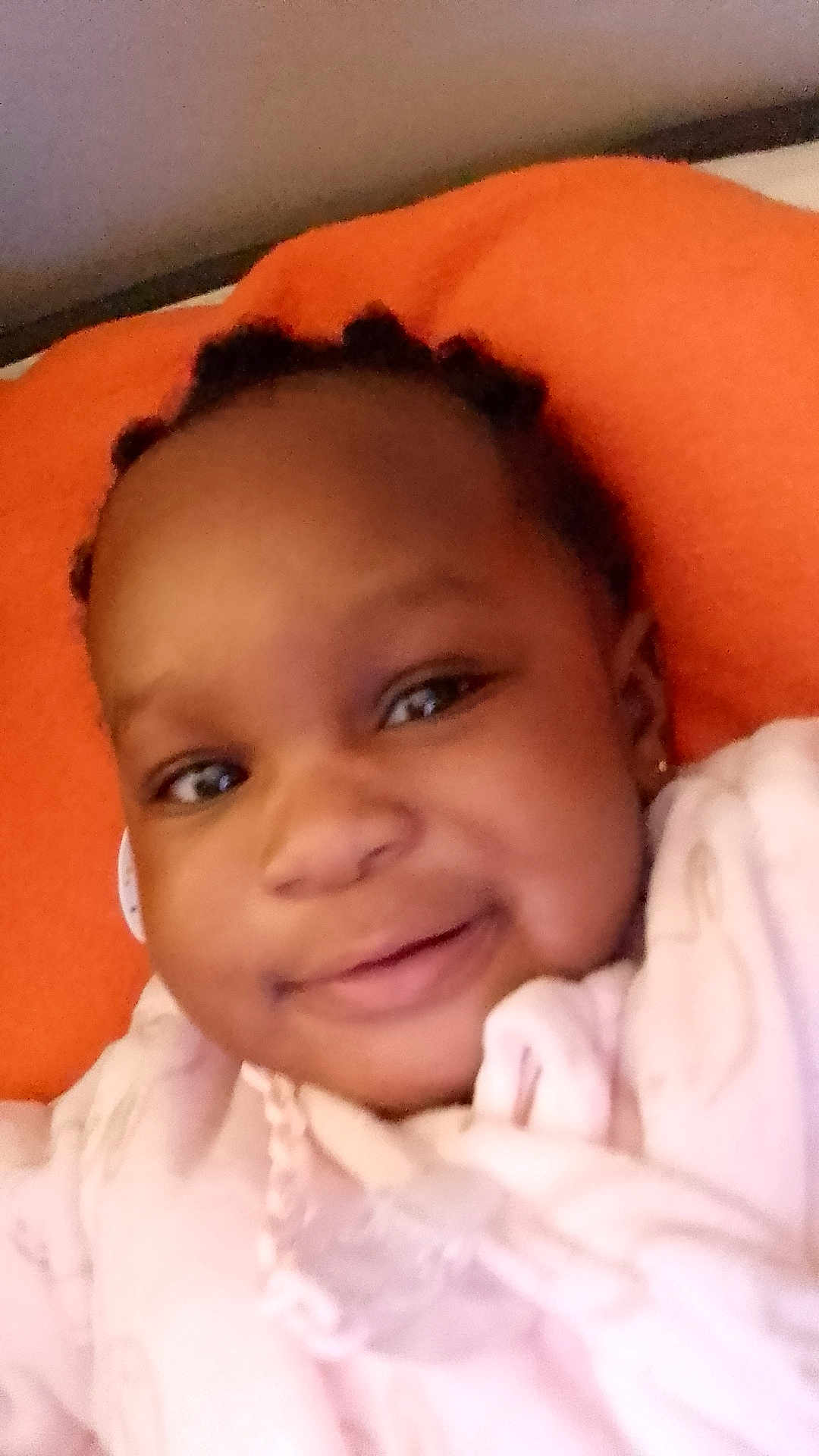 Iris a rejoint le concours — aidez-le/la à gagner de superbes lots ! baby, smile, face, child, infant, portrait, closeup, braids, cushion, orange, pink_clothing, necklace, earring, happy, indoors, person, cute, young_child, soft_lighting, resting