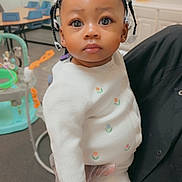 Jermanii joined the competition — help win amazing prizes! toddler, child, braids, beads, white_sweater, gloved_hand, indoor, classroom, educational_posters, toys, table, chair, cute, portrait, person, baby, curious, young_child, infant, holding