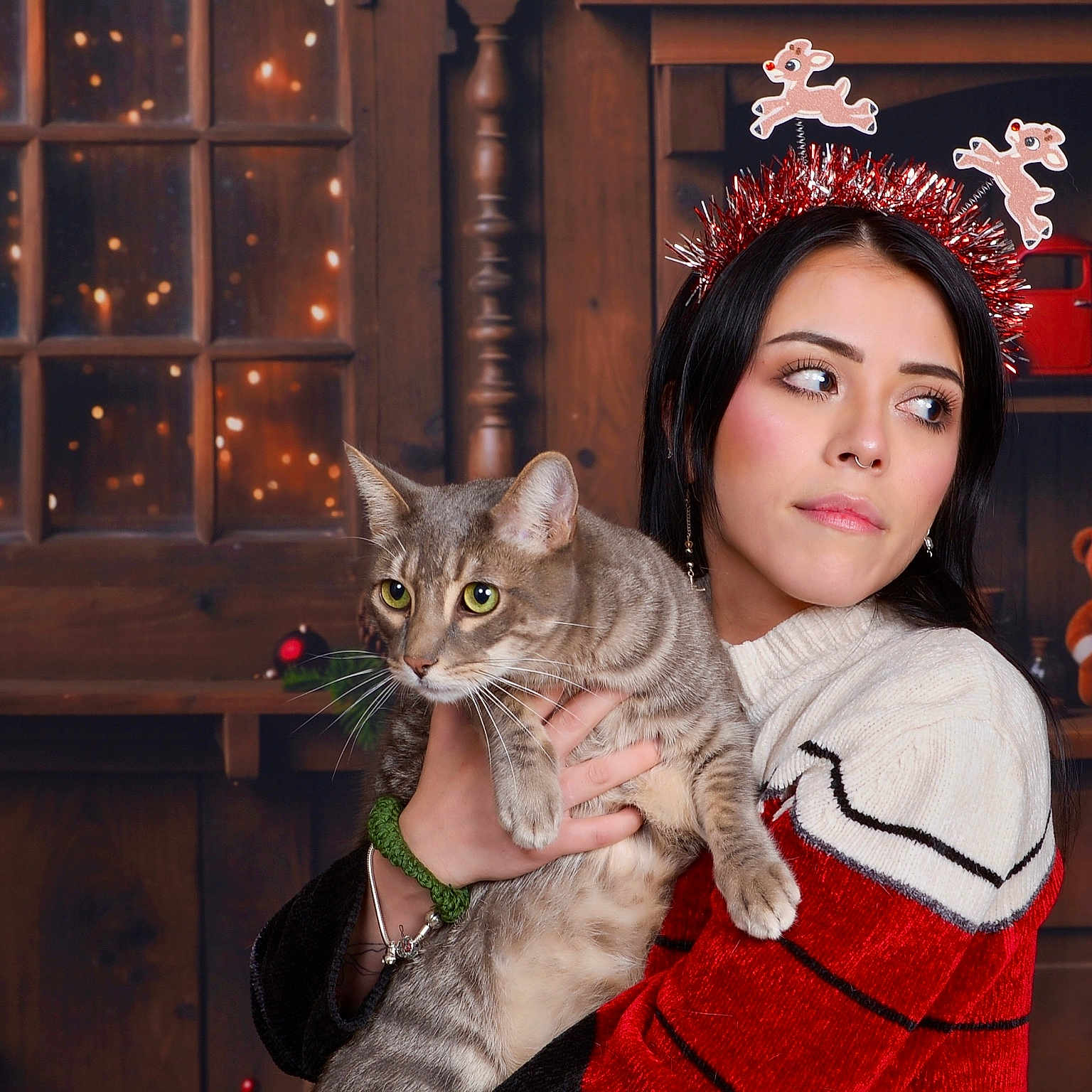 Nezuko Aka Nez is registered to the contest to win money with this photo: woman, cat, tabby_cat, holiday, christmas, festive, headband, reindeer, sweater, red, white, wooden_shelf, toy_truck, teddy_bear, window, lights, indoor, portrait, holding, decorations